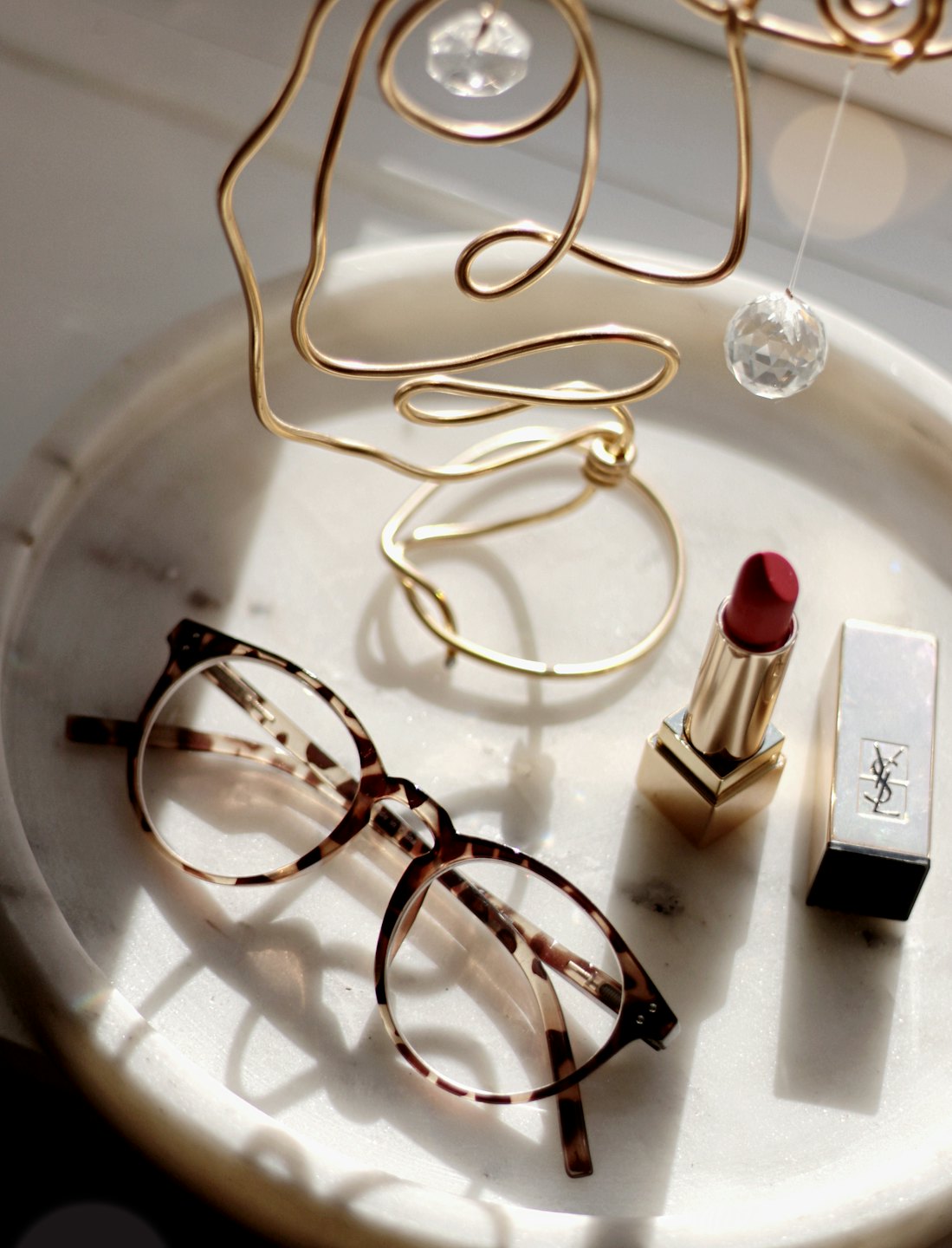 Eyeglasses, lipstick, and abstract art on marble tray.
